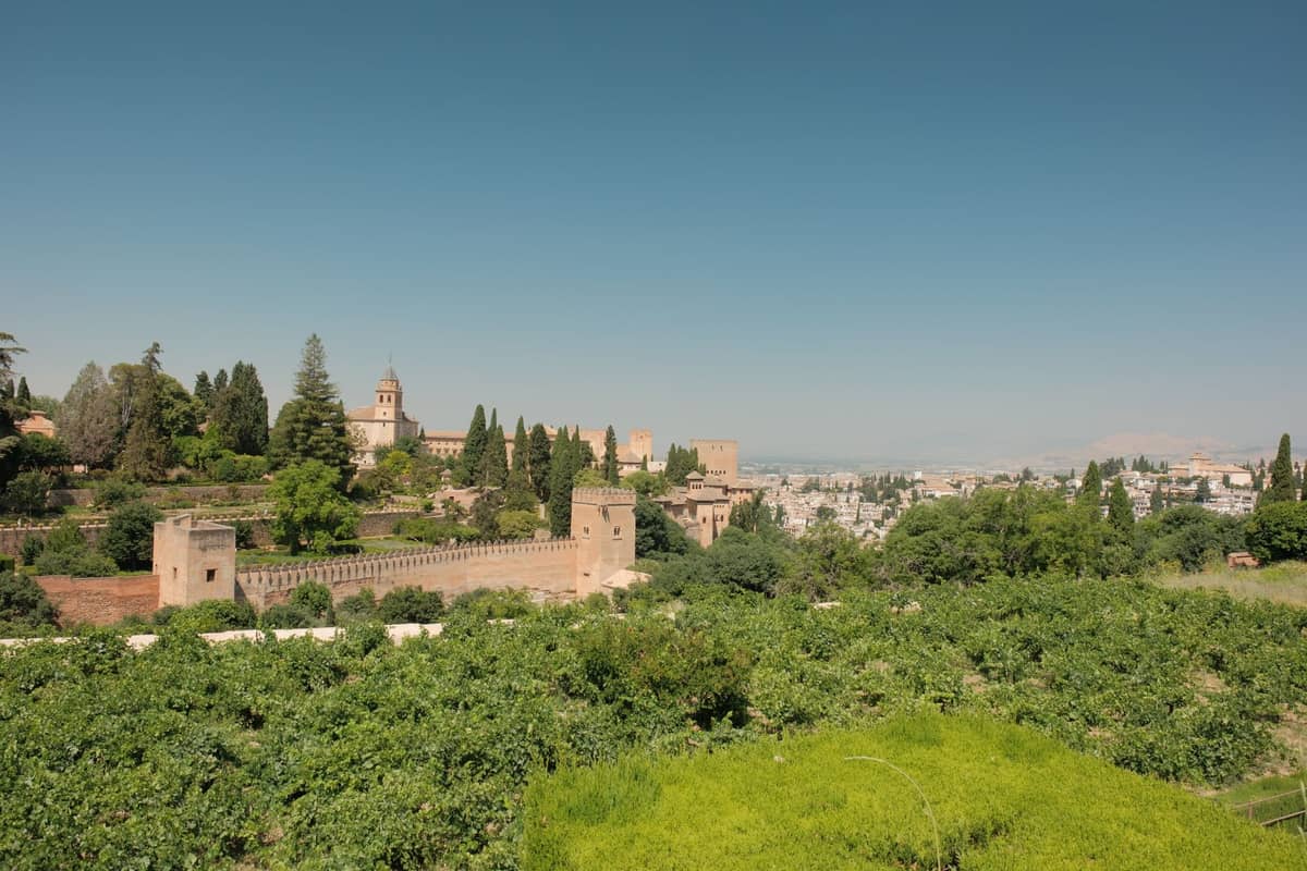 วิวทิวทัศน์ของ Alhambra และสวนสีเขียวขจีในเมือง Granada ประเทศสเปน พร้อมต้นไม้เขียวชอุ่มและท้องฟ้าสีฟ้าใสในฤดูใบไม้ผลิ