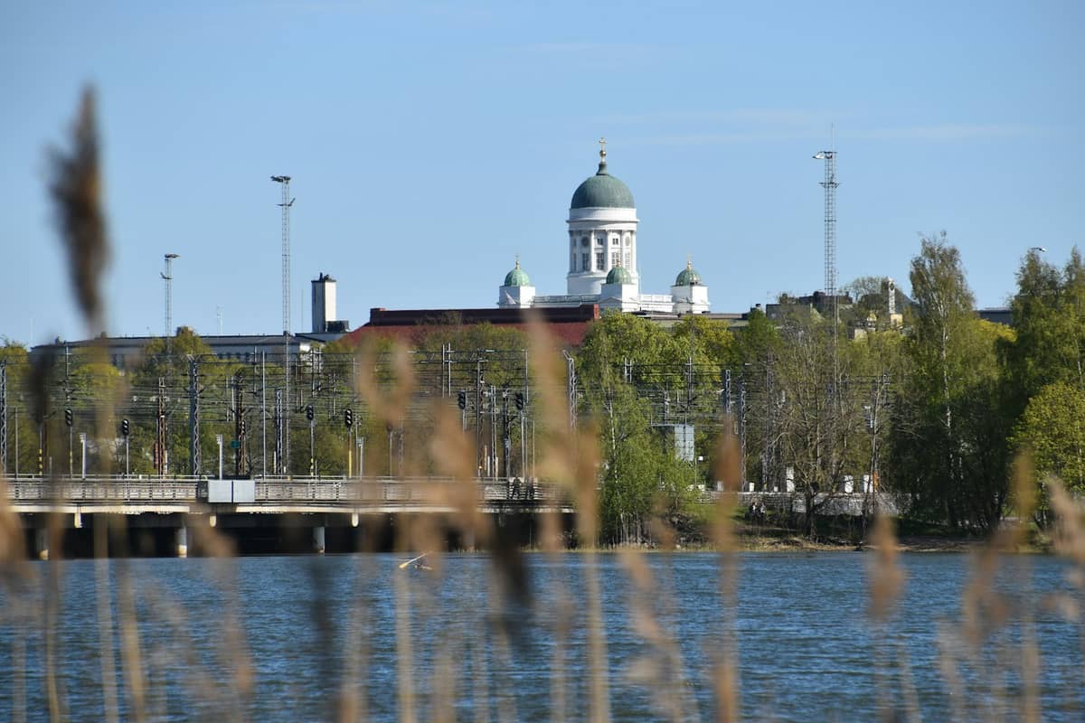 Vista sobre a água para a Catedral de Helsinque com árvores começando a verdejar, mostrando o início lento da primavera em Helsinque.