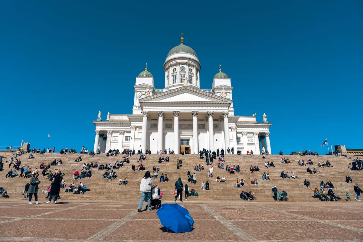Multidões relaxando e sentadas nos degraus em frente à Catedral de Helsinque sob um céu azul limpo de primavera ou início de outono.