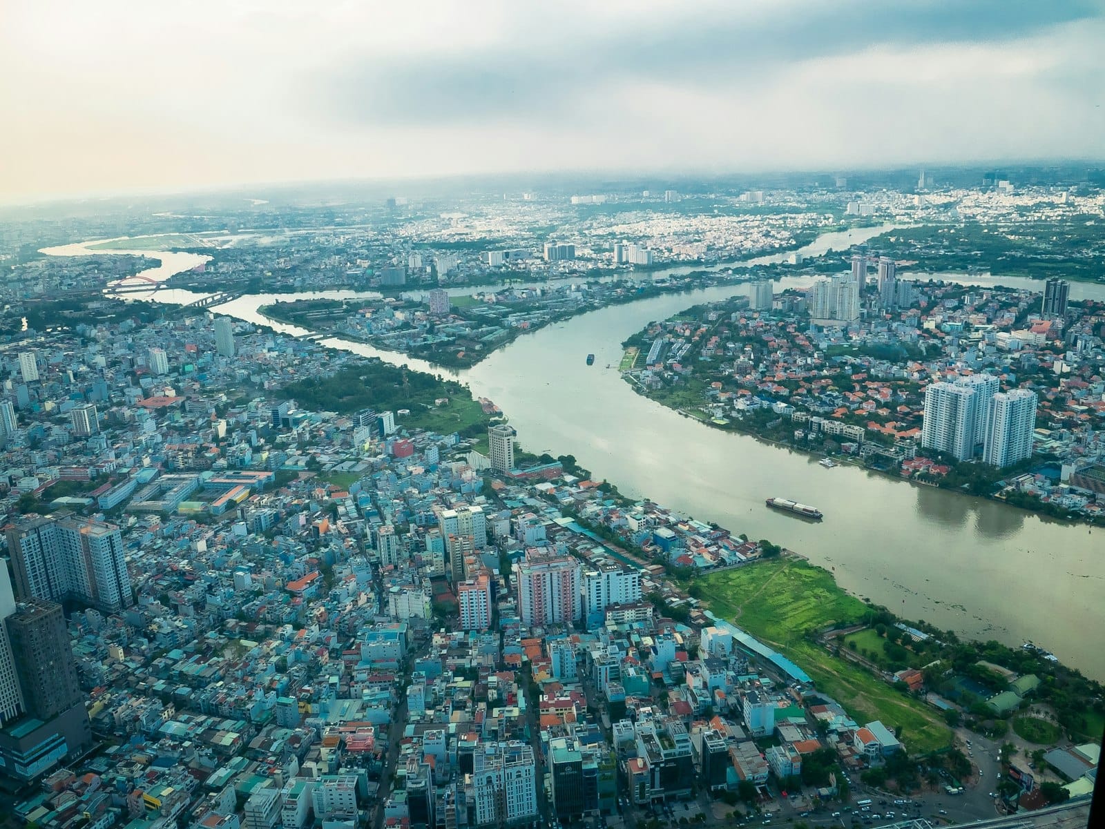 Vista aérea de Ho Chi Minh City con el río Saigon serpenteando entre densos barrios urbanos bajo un cielo parcialmente nublado.