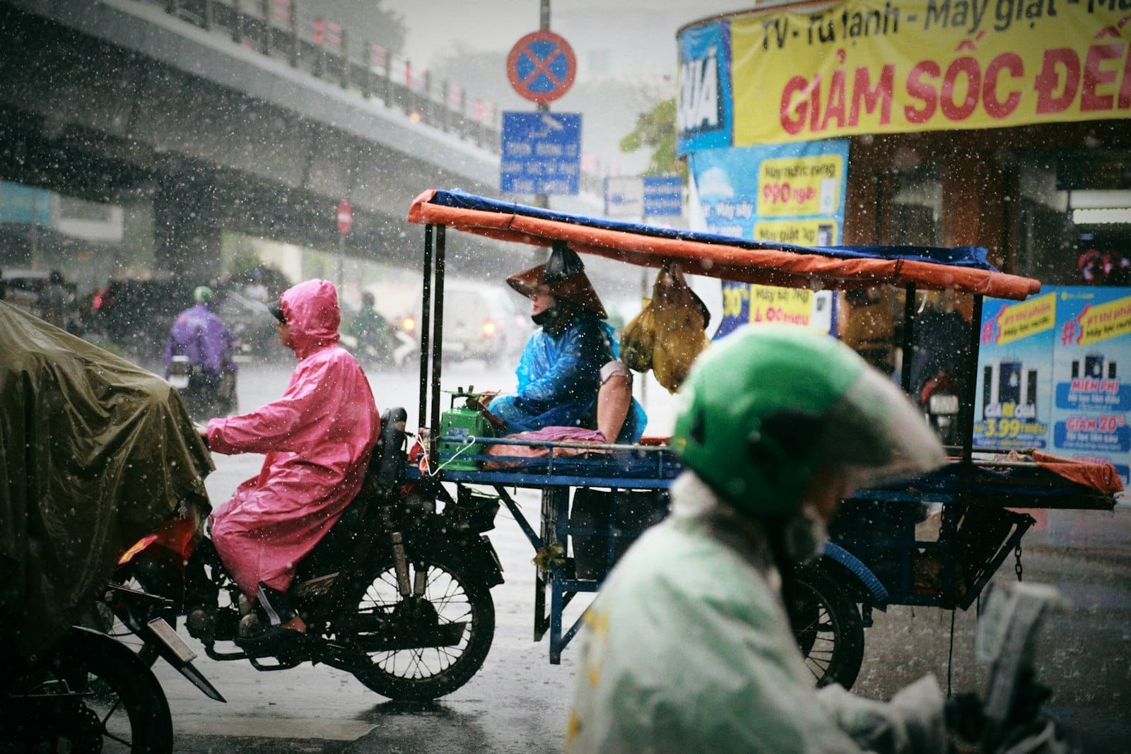 Personas con impermeables montan motocicletas junto a un puesto de comida callejera bajo una fuerte lluvia en Ho Chi Minh City.