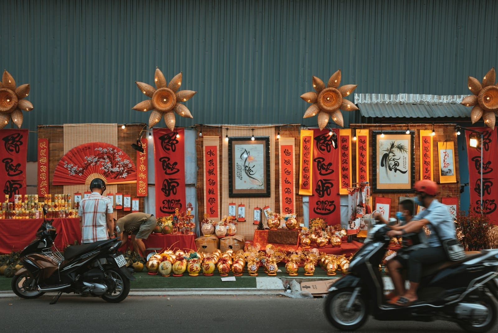 Calle decorada con pancartas rojas, adornos dorados y elementos temáticos del Tet, con scooters pasando por delante.
