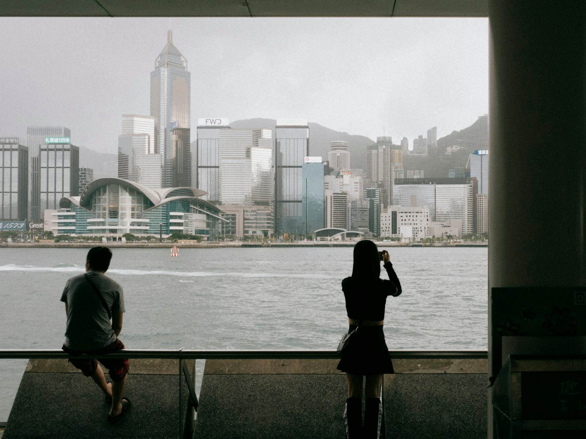 Pessoas no porto de Hong Kong sob céu nublado com skyline ao fundo