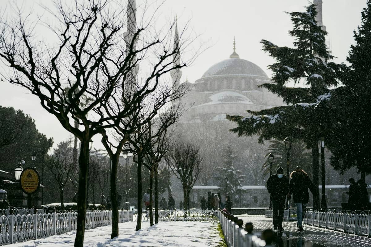 Persone che camminano accanto ad alberi coperti di neve verso la Hagia Sophia a Istanbul in una giornata invernale.