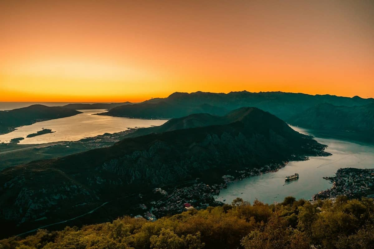 Dramatic sunset view over the Bay of Kotor with golden autumn light and a cruise ship in the water, surrounded by mountains.