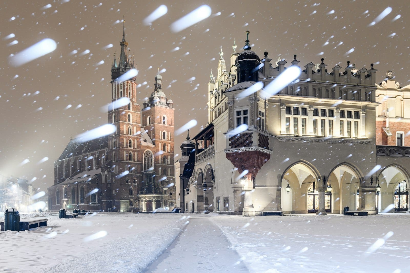 จัตุรัส Rynek Główny ในเมือง Kraków ปกคลุมด้วยหิมะในยามค่ำคืน วิหาร มหาวิหารเซนต์แมรี่ และ อาคาร Sukiennice สว่างไสว พร้อมหิมะตกหนัก