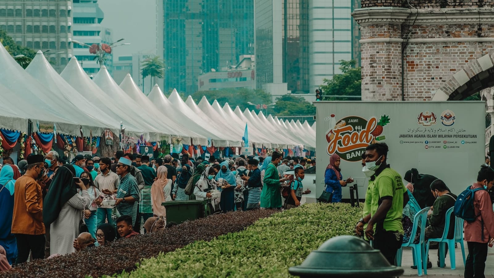 Large crowd enjoying a food festival under white tents in central Kuala Lumpur, with city skyscrapers and greenery in the background.