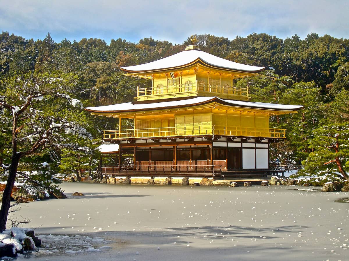 Kinkaku-ji Golden Pavilion in Kyoto surrounded by snow and a frozen pond in winter, with trees dusted in snow.