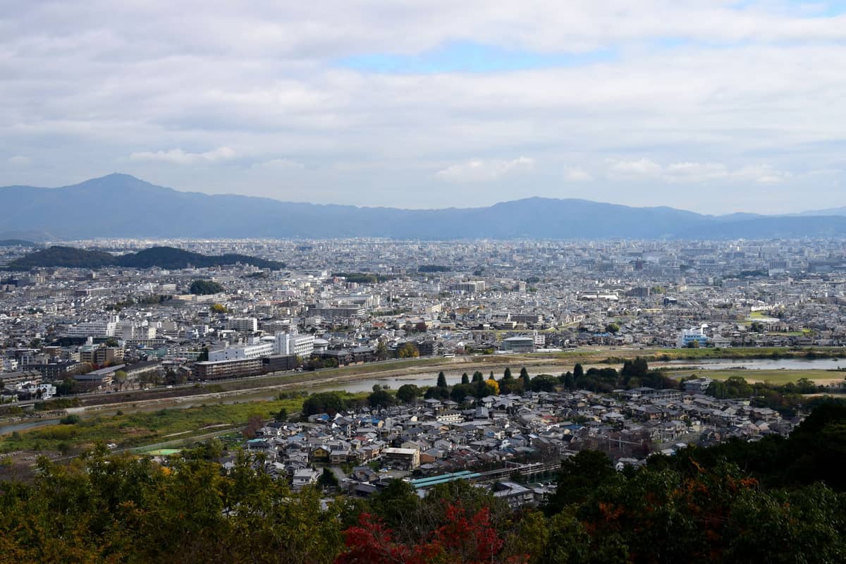 Panoramic view of Kyoto city with encircling mountains, river, and urban landscape under a partly cloudy sky