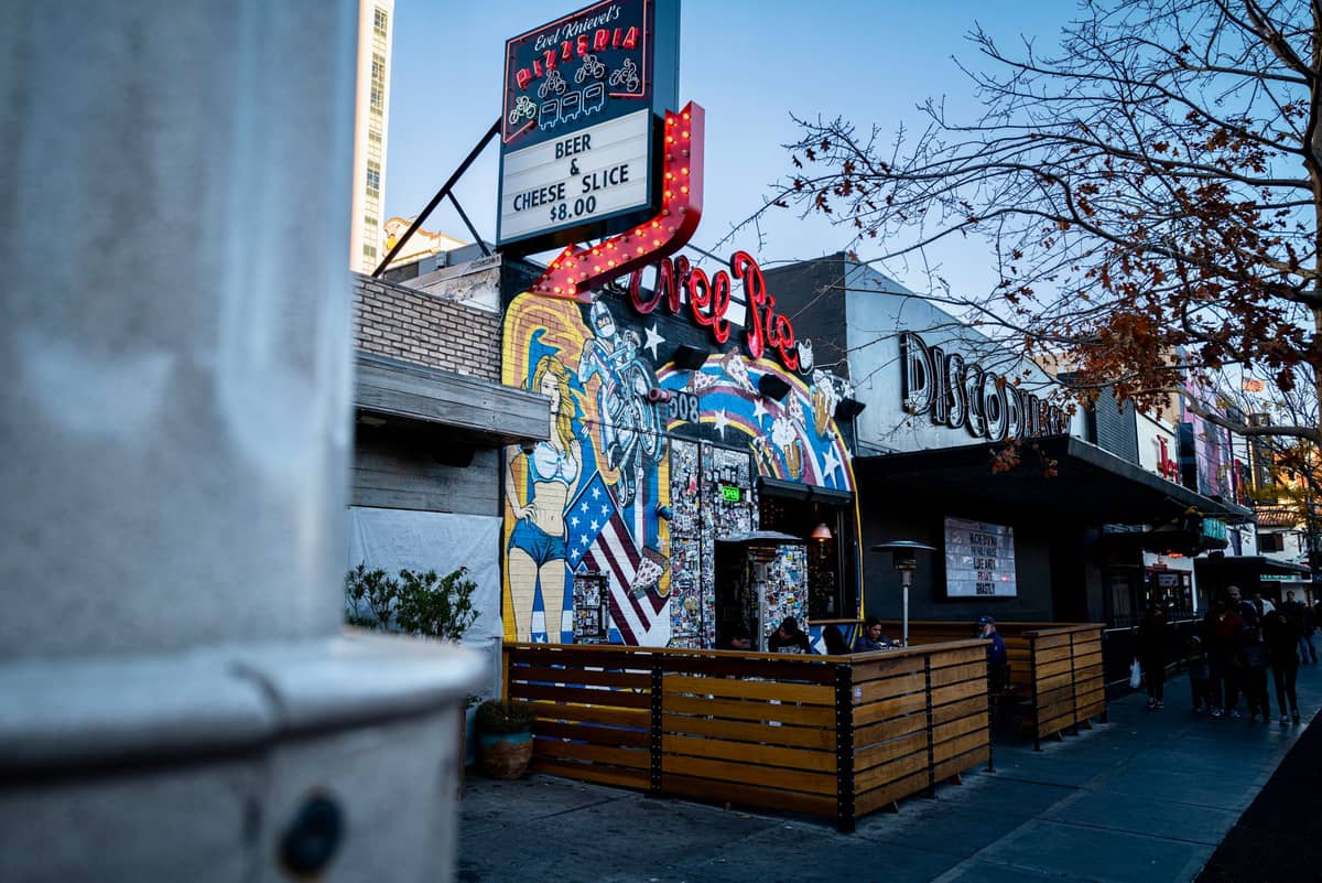 Street view of a lively bar and restaurant with autumn leaves on the tree, outdoor patio, and people walking in downtown Las Vegas.
