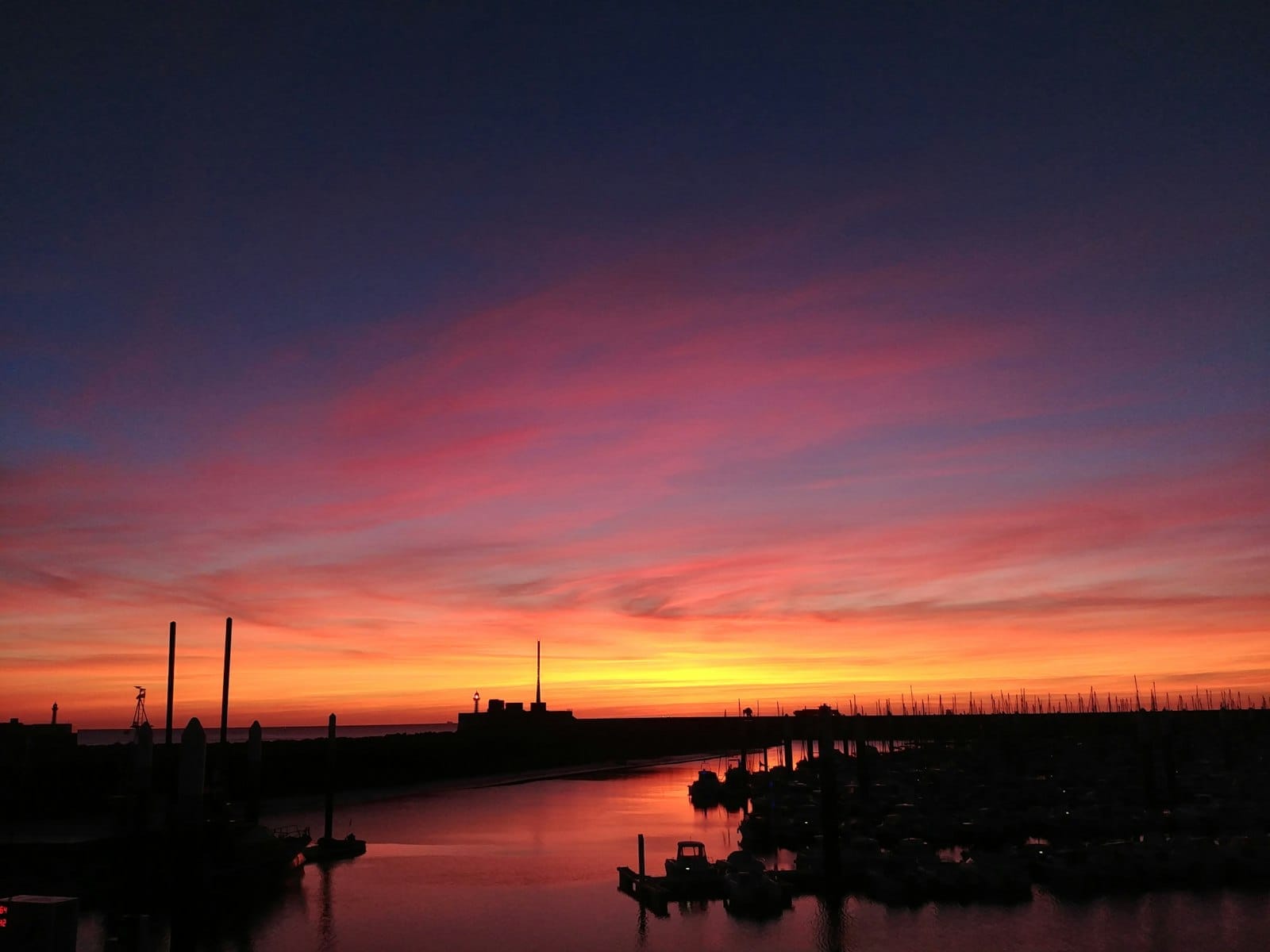 Le Havre harbor at sunset with vibrant autumn colors in the sky and boats in silhouette, creating a warm, golden evening atmosphere.