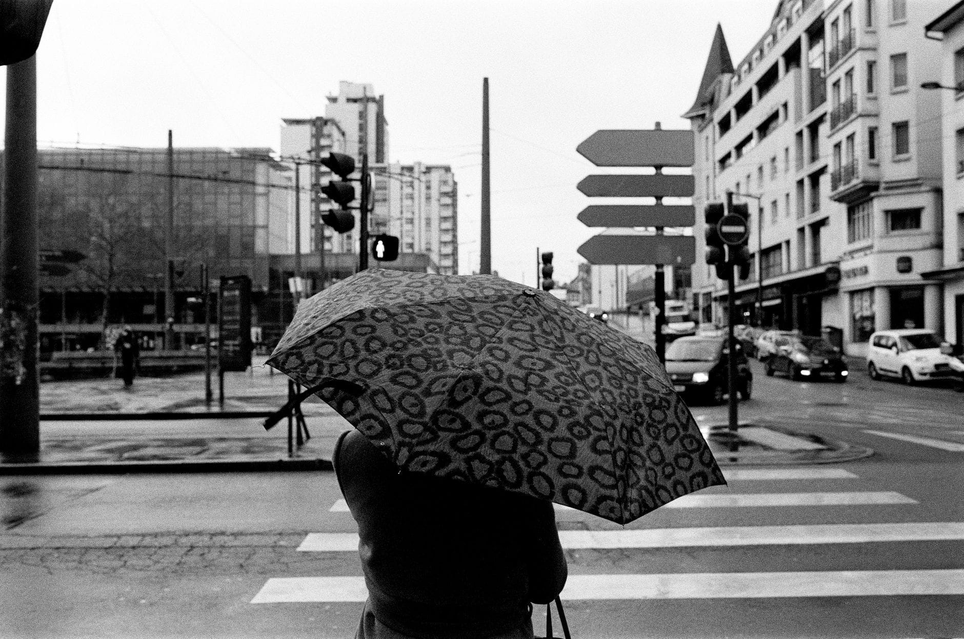 Person with umbrella crossing a wet intersection in a modern French city on a gray winter day