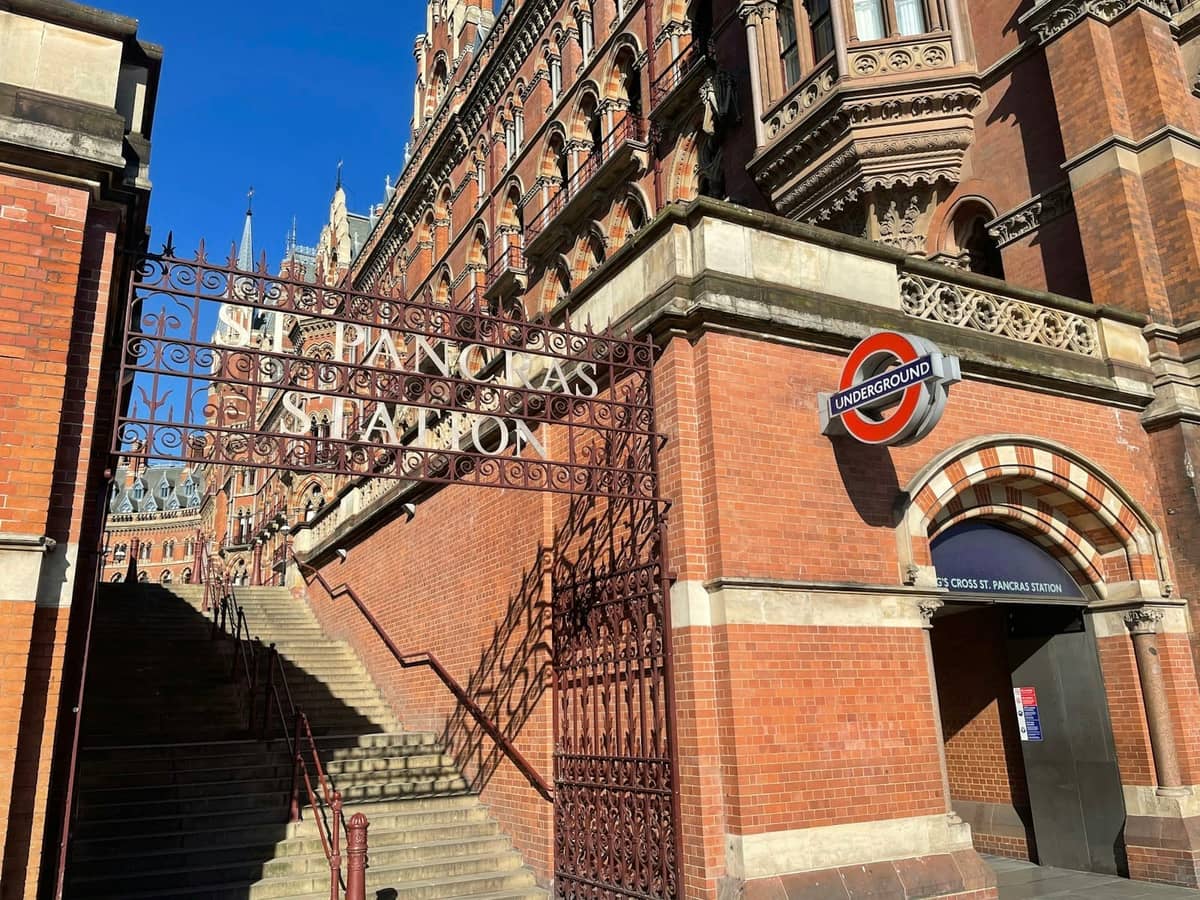 Vista da entrada da St Pancras Station em Londres com arquitetura em tijolo vermelho e placa do Underground sob um céu azul limpo