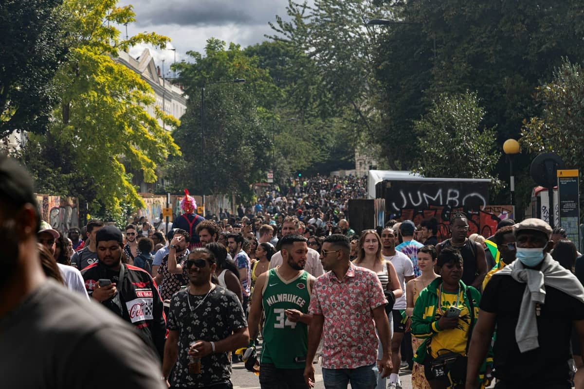 Grande multidão de pessoas participando de um animado evento de rua em Londres com árvores e prédios da cidade ao fundo.