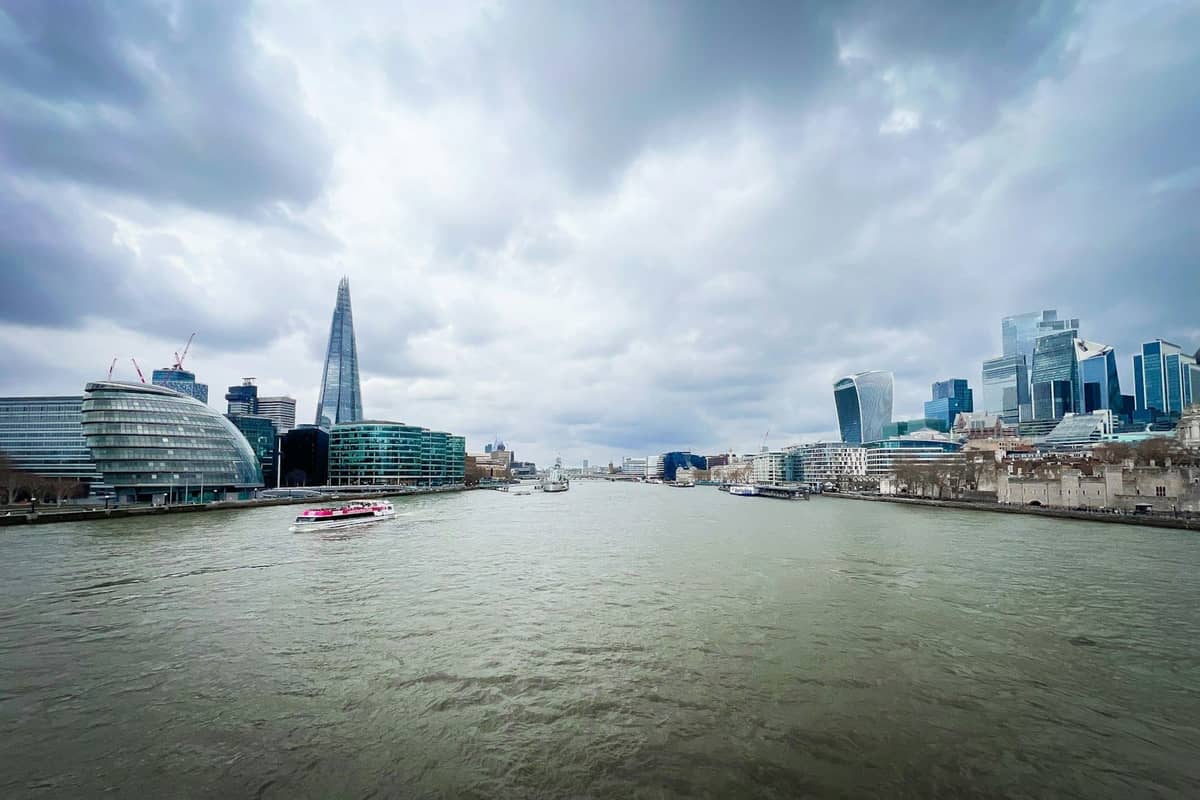 Vista ampla do rio Tâmisa em Londres com o horizonte moderno da cidade, céu nublado e o arranha-céu Shard visível.