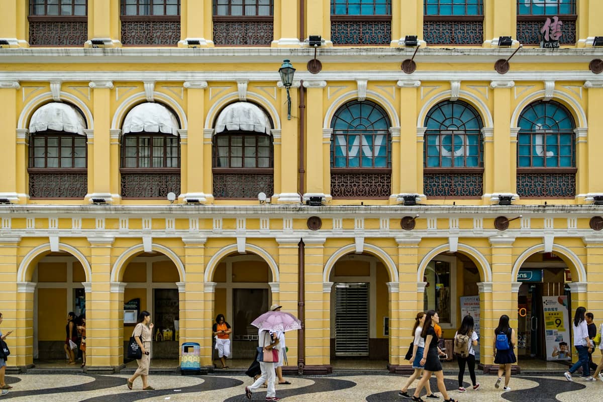 Fußgänger, die an einem klaren Tag vor der historischen gelben Kolonialarkade am Senado Square, Macau, spazieren.