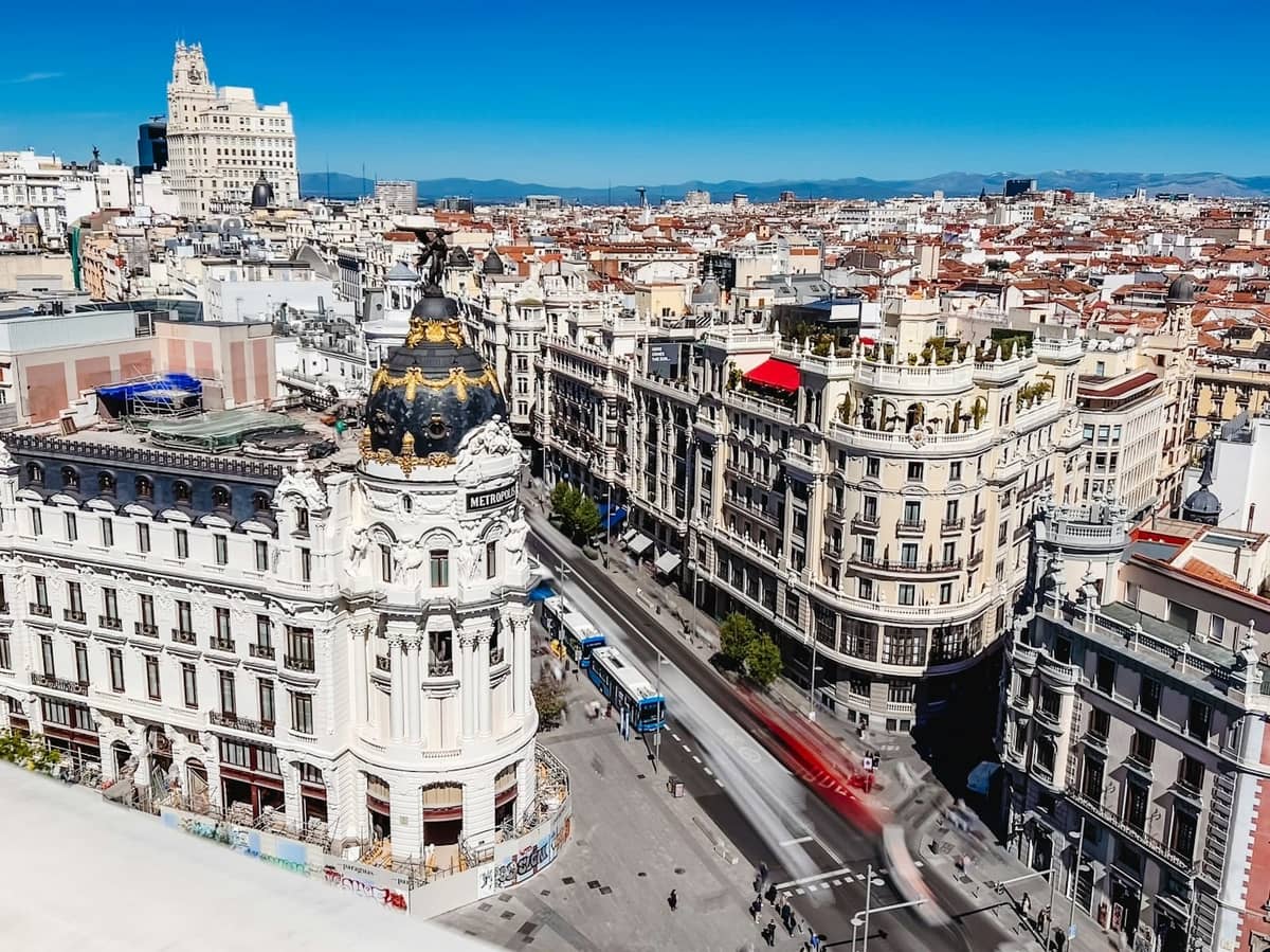 Vista aerea della Gran Vía di Madrid con cieli blu limpidi, edifici storici e tetti della città che si estendono fino alle montagne lontane.