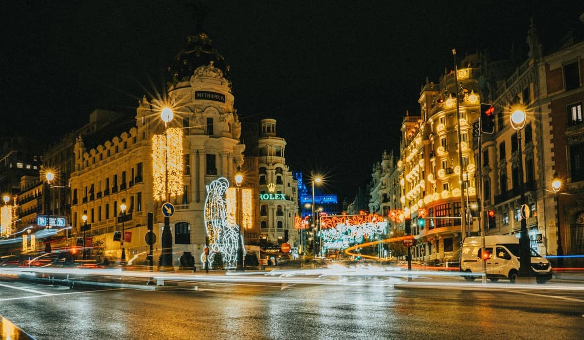 Vista notturna della Gran Vía di Madrid e dell'edificio Metrópolis illuminati con luci e decorazioni festive invernali.
