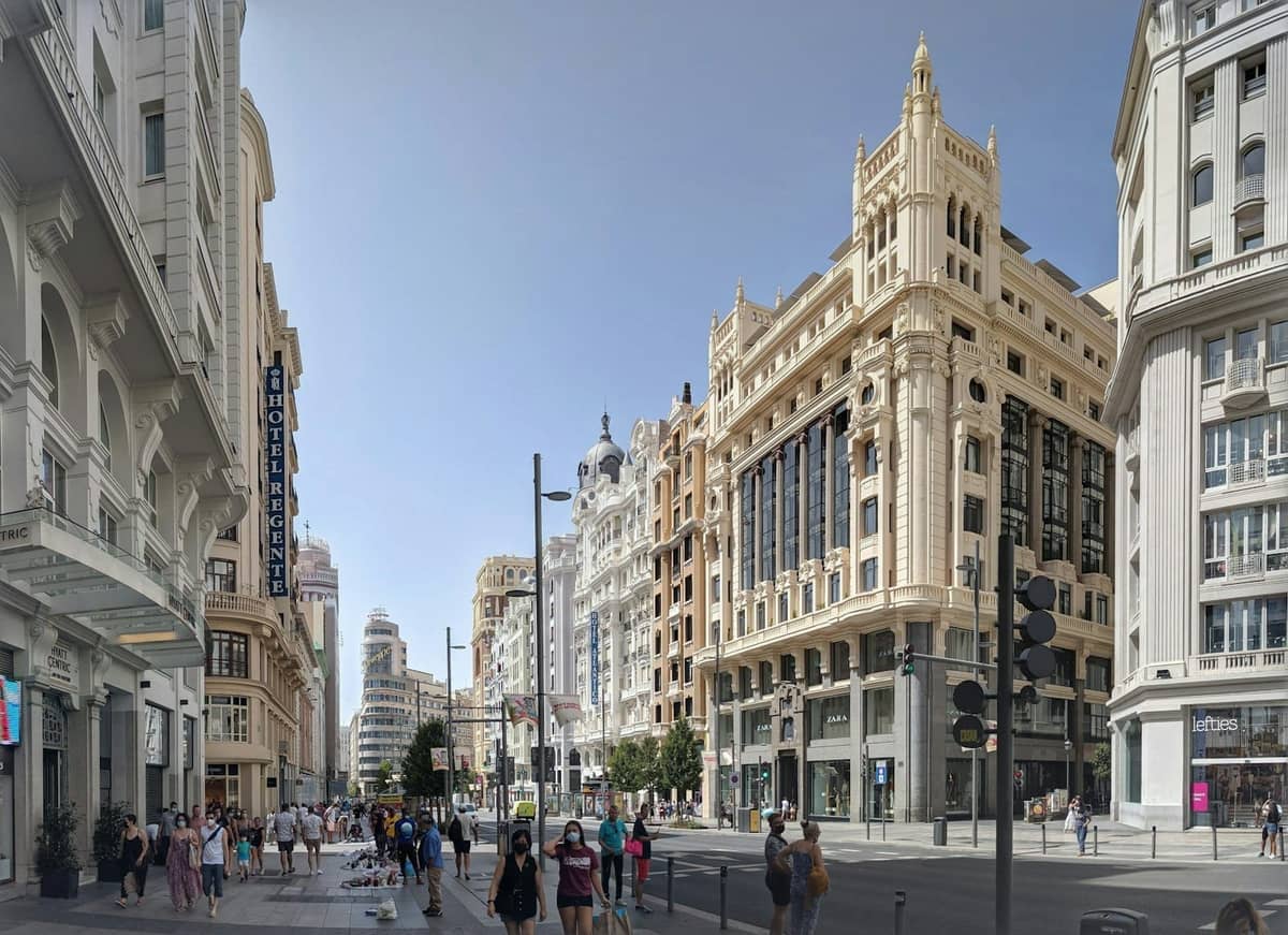 Una strada affollata e soleggiata a Madrid con persone che passeggiano sotto cieli sereni e un'architettura urbana classica, che illustra la vivace atmosfera estiva della città.