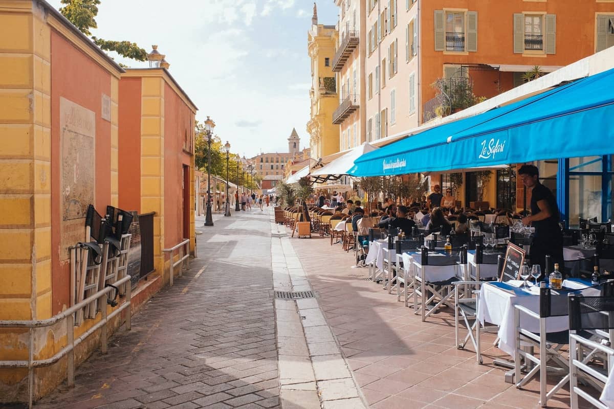 Jadalnia na świeżym powietrzu w tętniącej życiem restauracji na Majorce z niebieskim markizem, usytuowana przy słonecznej ulicy otoczonej kolorowymi śródziemnomorskimi budynkami.
