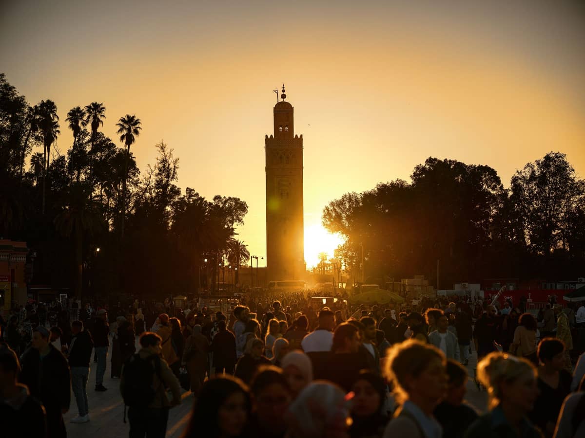 ฝูงชนรวมตัวกันที่จัตุรัส Jemaa el-Fnaa ในเมือง Marrakech ยามพระอาทิตย์ตก โดยมีเงาสีดำของมัสยิด Koutoubia และต้นปาล์มตัดกับท้องฟ้าสีทอง
