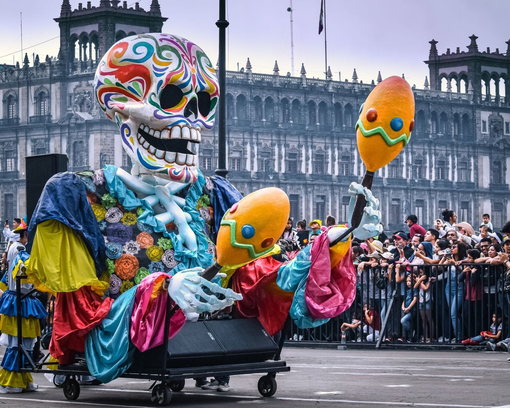 Grande carro alegórico com esqueleto colorido desfilando diante da multidão no Zócalo da Cidade do México, durante uma grande celebração do Día de Muertos.