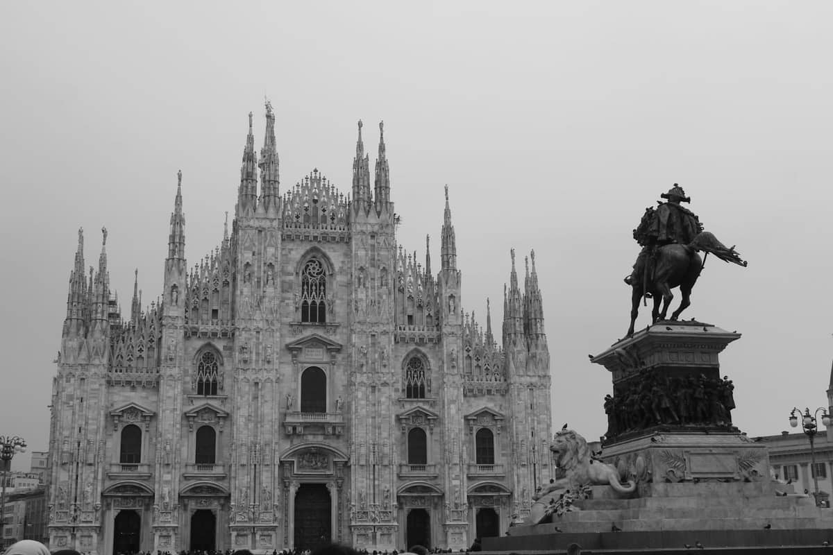 Foto in bianco e nero del Duomo di Milano e di una statua equestre in un'atmosfera nebbiosa e invernale con cielo coperto.