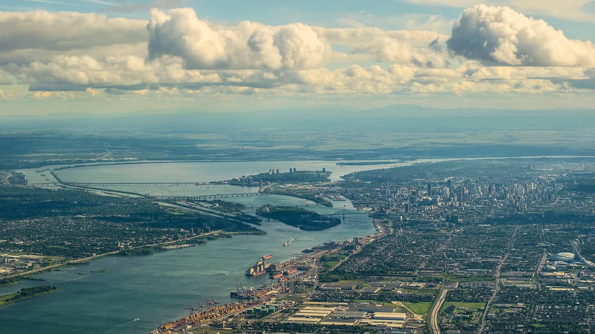 Luftaufnahme von Montreal mit der Insel, der Stadt, dem Sankt-Lorenz-Strom und zusammenlaufenden Wasserwegen unter einem teils bewölkten Himmel.