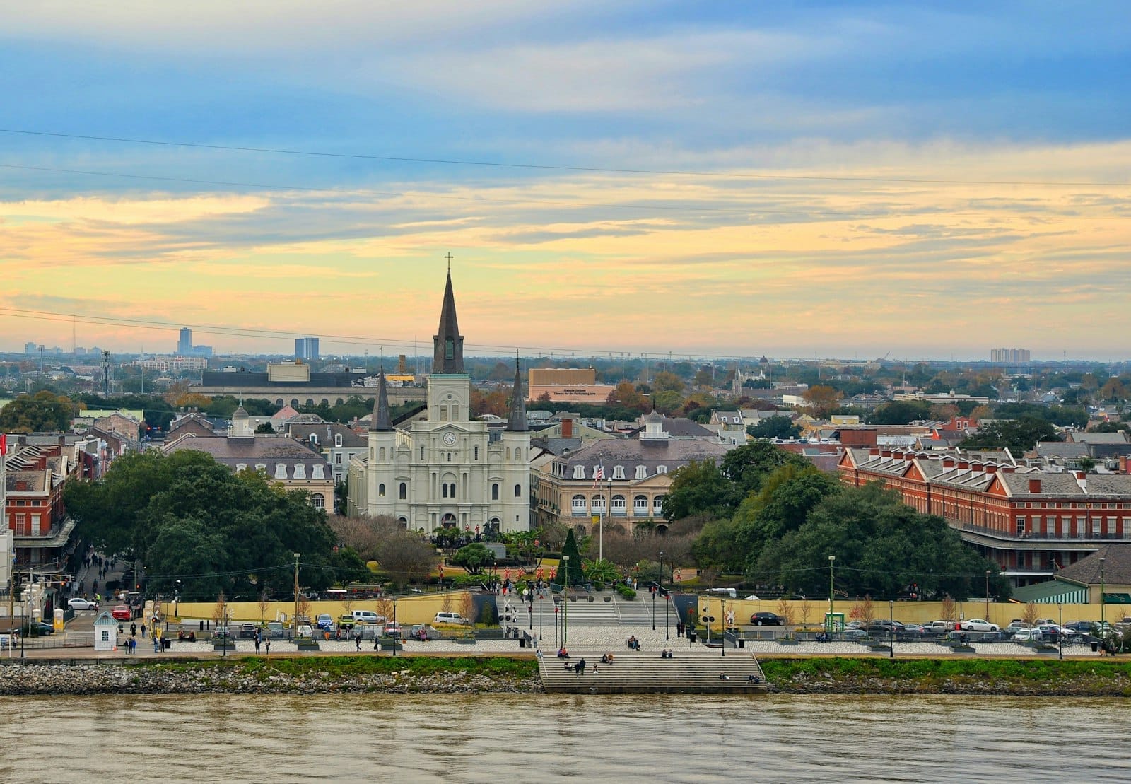 Vista panorâmica da Jackson Square e da Catedral de São Luís com prédios históricos e o Rio Mississippi sob um céu colorido em Nova Orleans.