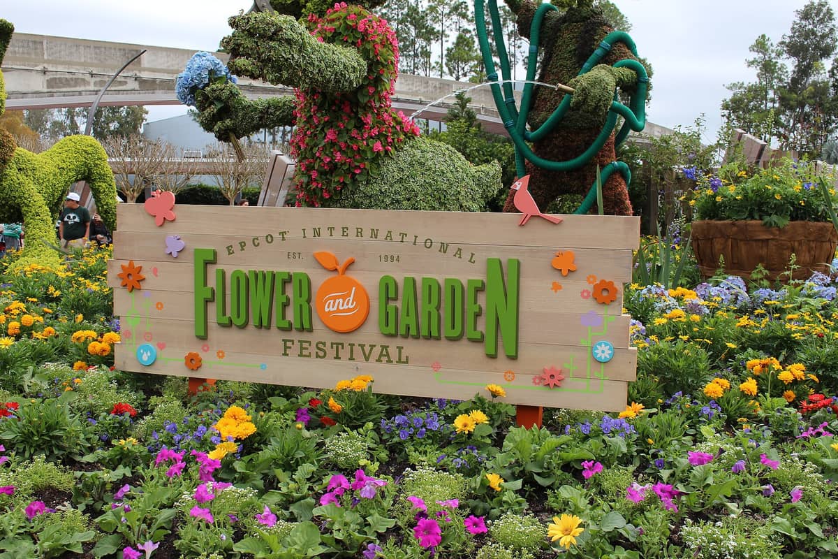 Schild des Epcot International Flower and Garden Festival, umgeben von bunten Blumen und Figuren-Topiaren im Epcot in Orlando.