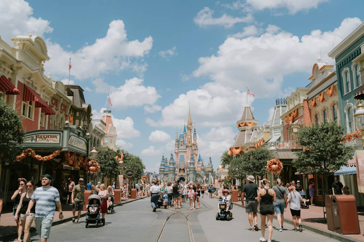 Wide view down Main Street USA at Magic Kingdom with Cinderella Castle in the background, crowds of visitors, sunny sky and classic theme park atmosphere.