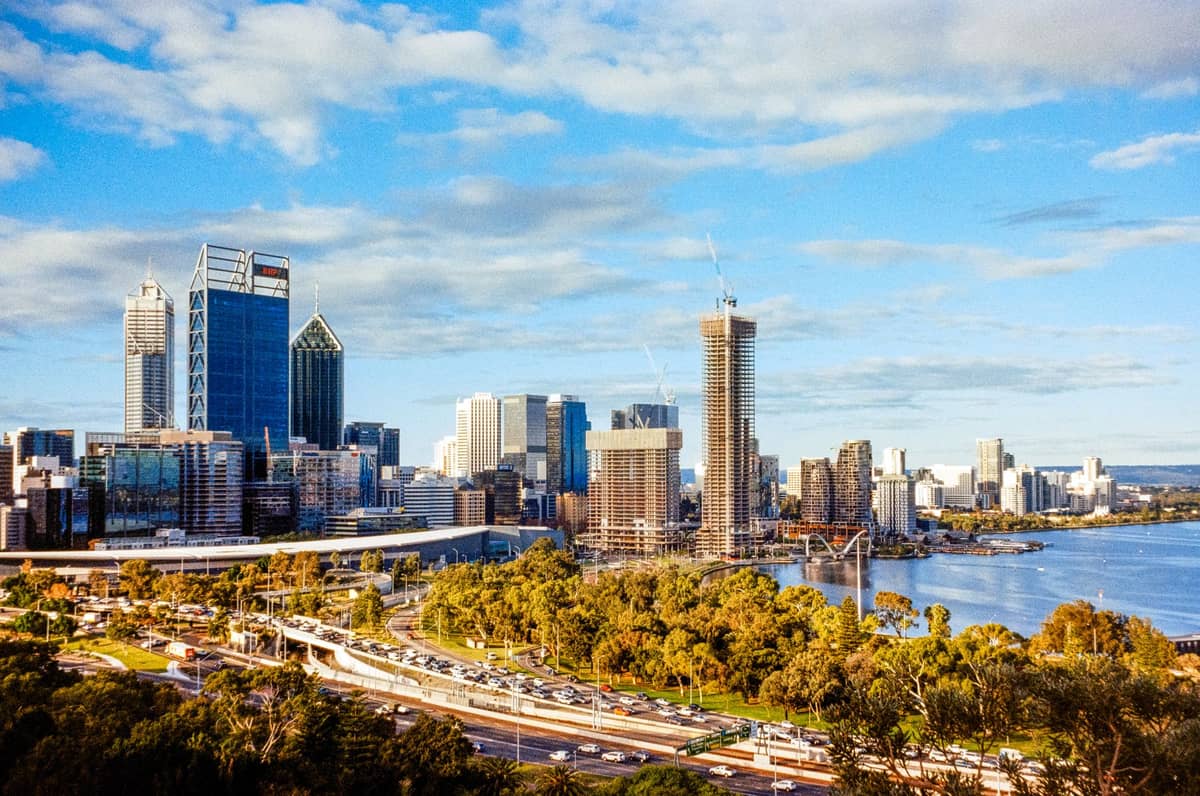 Vista luminosa e soleggiata dello skyline di Perth con cielo azzurro, grattacieli e il fiume Swan in primo piano.