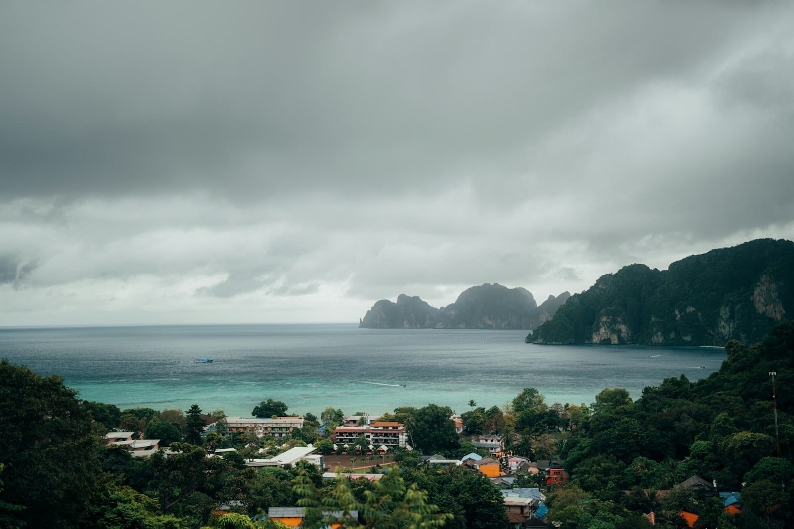 Dramatic cloudy sky over a coastal town in Phuket with green hills and turquoise water, suggesting monsoon season weather.
