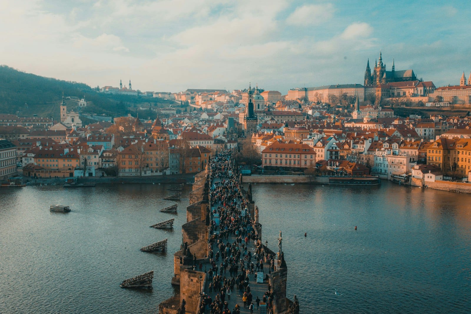 Luftaufnahme der Karlsbrücke in Prag voller Menschen, mit der Moldau und der historischen Stadtsilhouette im Hintergrund.