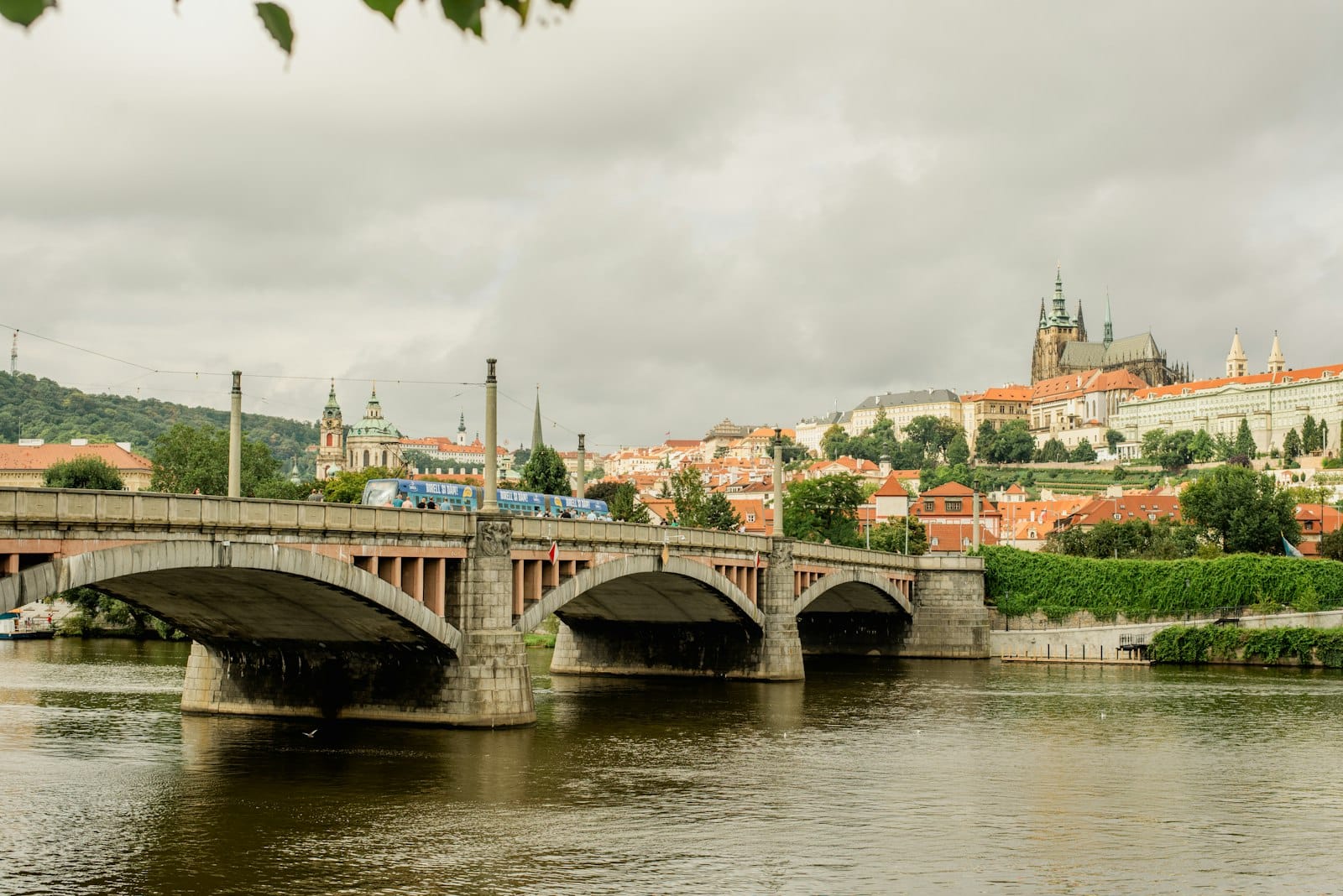 Brücke mit Straßenbahn über die Moldau und Blick auf die Prager Burg und Stadtgebäude im Hintergrund