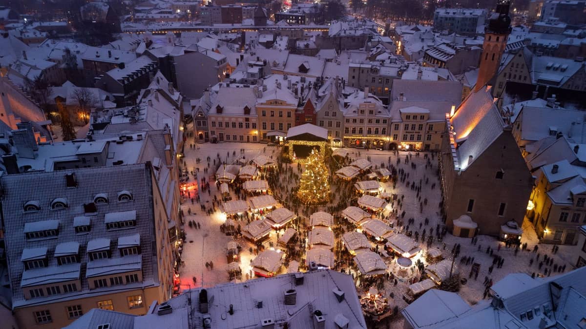 Luftaufnahme der Rigaer Altstadt mit einem belebten Weihnachtsmarkt und schneebedeckten Dächern in der Abenddämmerung.