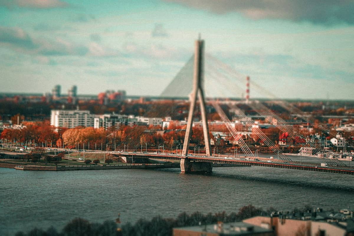 Landschaftsansicht der Schrägseilbrücke von Riga und der Stadtsilhouette mit Bäumen in Herbstfarben entlang des Flussufers.