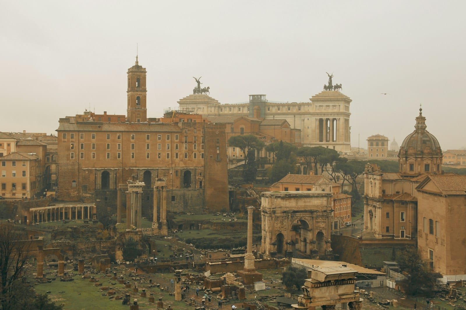 Moody winter scene of the Roman Forum in Rome with overcast skies and famous ancient ruins prominently visible.