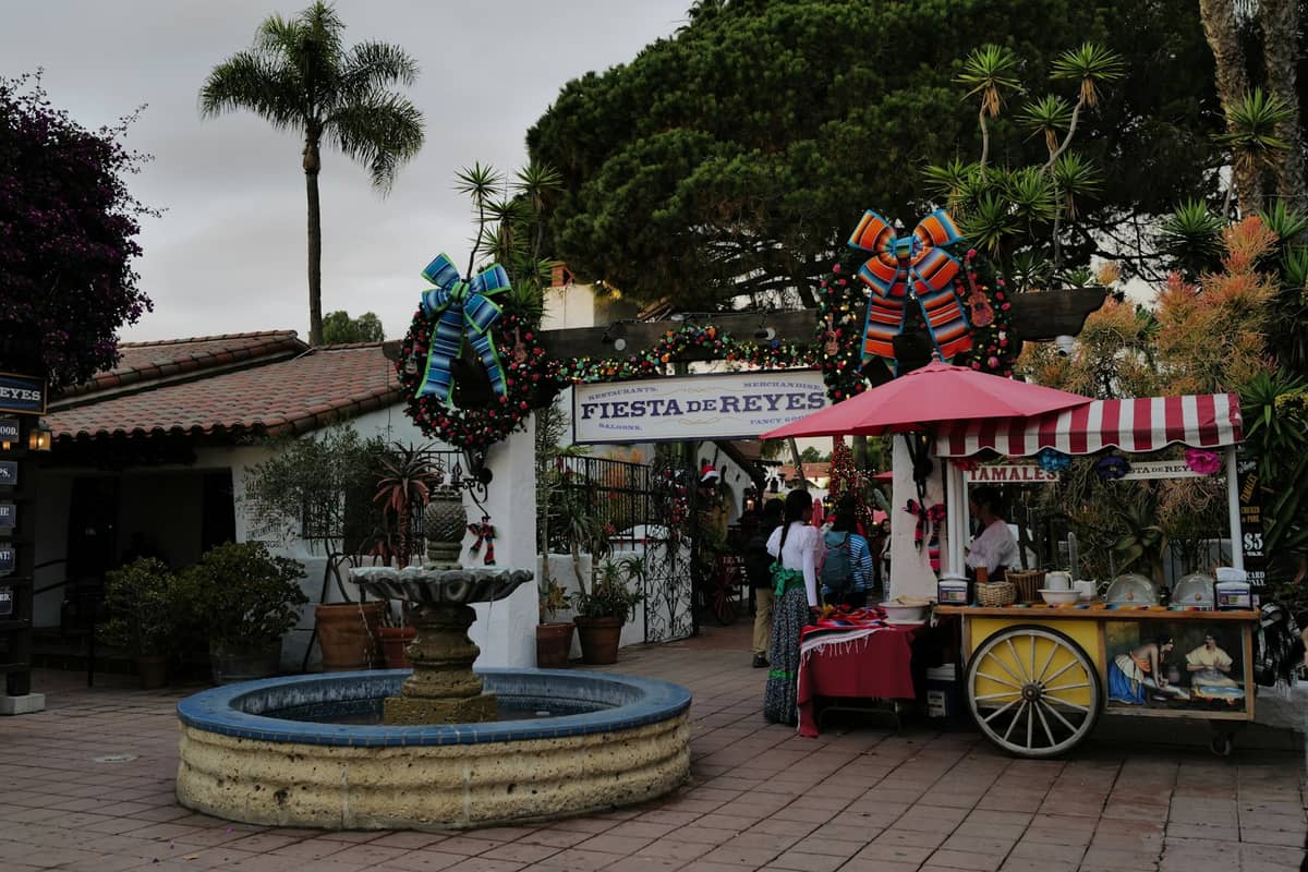 ลานเทศกาลที่ Fiesta de Reyes ใน Old Town San Diego พร้อมการตกแต่งวันหยุดและผู้คนเดินผ่านน้ำพุ