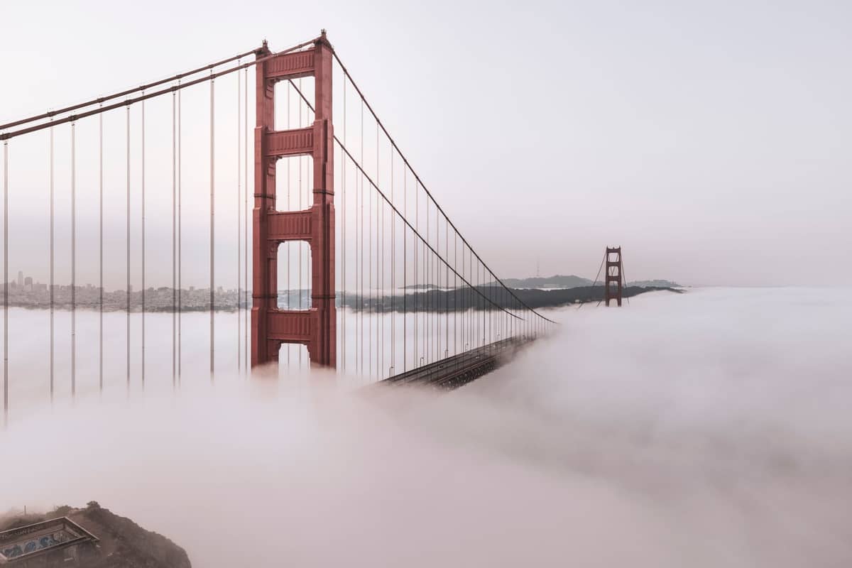 Die Golden Gate Bridge ragt aus dichtem Nebel hervor, wobei ein Großteil der Struktur und der Stadt von einer Meeresnebelschicht verdeckt wird, was das berühmte Klima von San Francisco veranschaulicht.