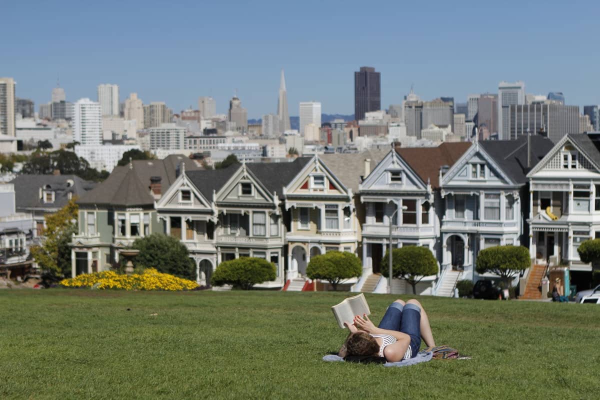 Person entspannt sich auf dem Rasen im Alamo Square Park mit Blick auf die Painted Ladies und die Skyline von San Francisco an einem klaren Frühlingstag