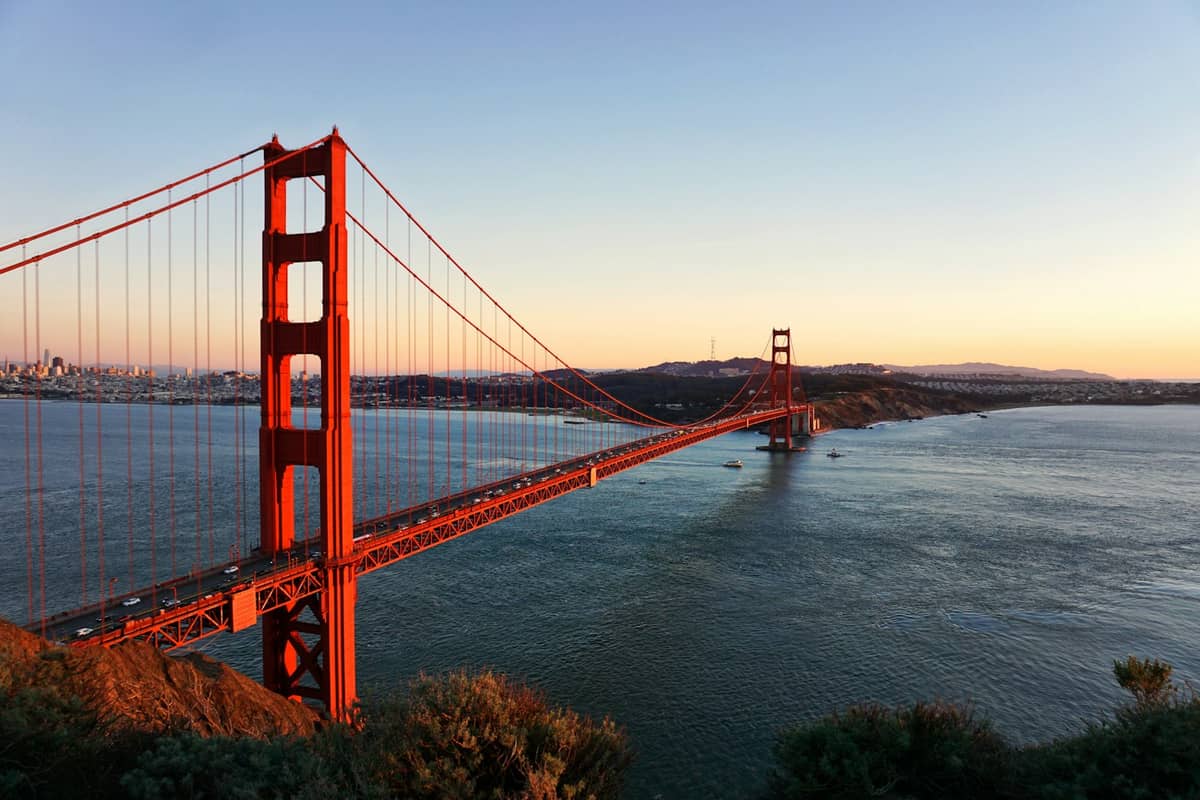Vista panorámica del puente Golden Gate al atardecer con aguas tranquilas y cielo despejado, el emblema de San Francisco.