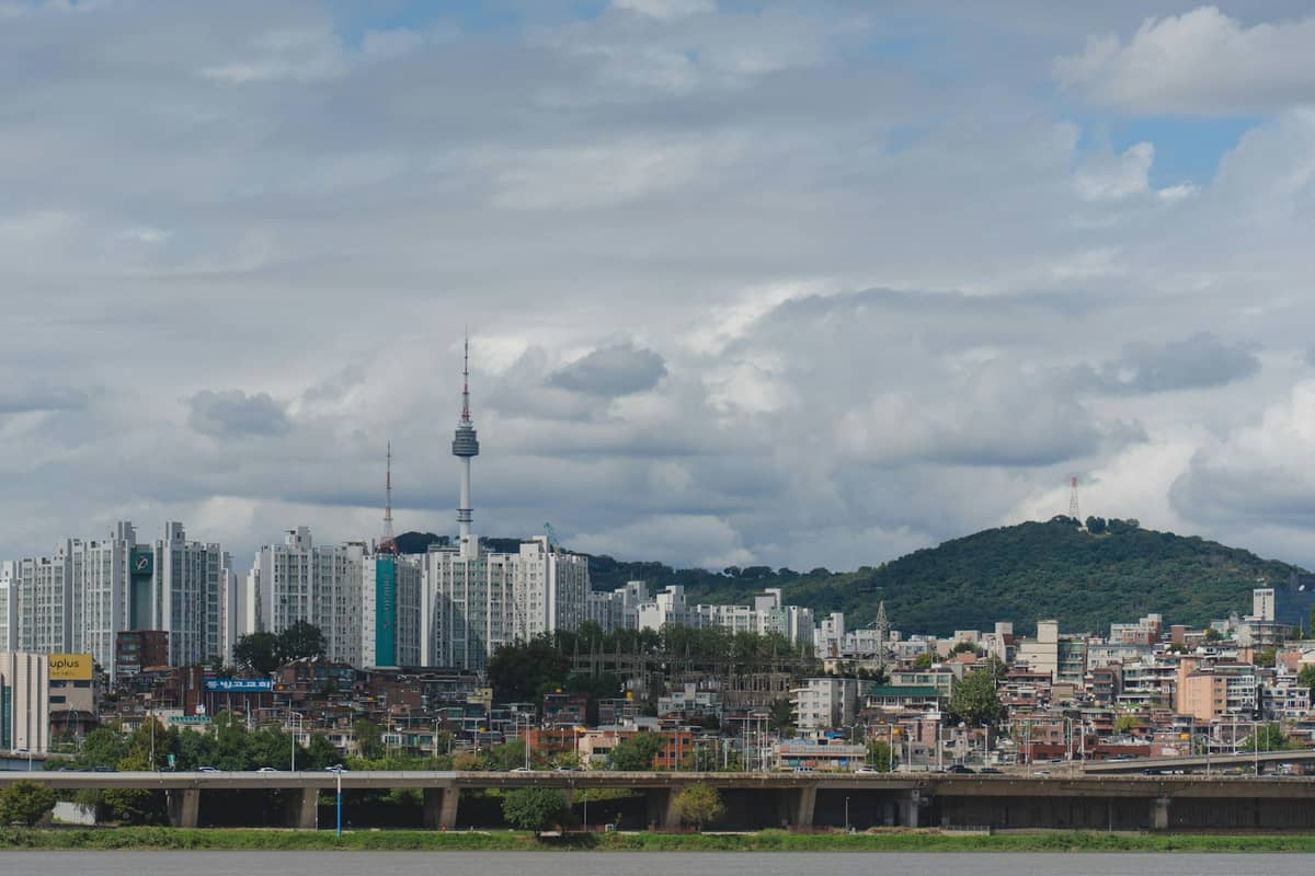 Horizonte de Seul com a Namsan Seoul Tower, edifícios modernos, o rio Han em primeiro plano e um céu dramático com nuvens.