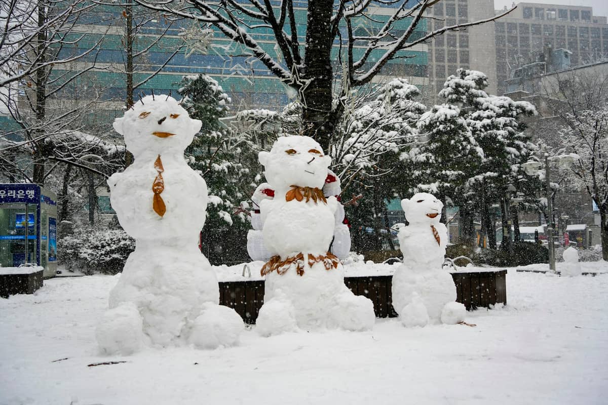 Três grandes bonecos de neve em um parque urbano em Seul, edifícios e árvores cobertos de neve fresca, capturando um frio dia de inverno.