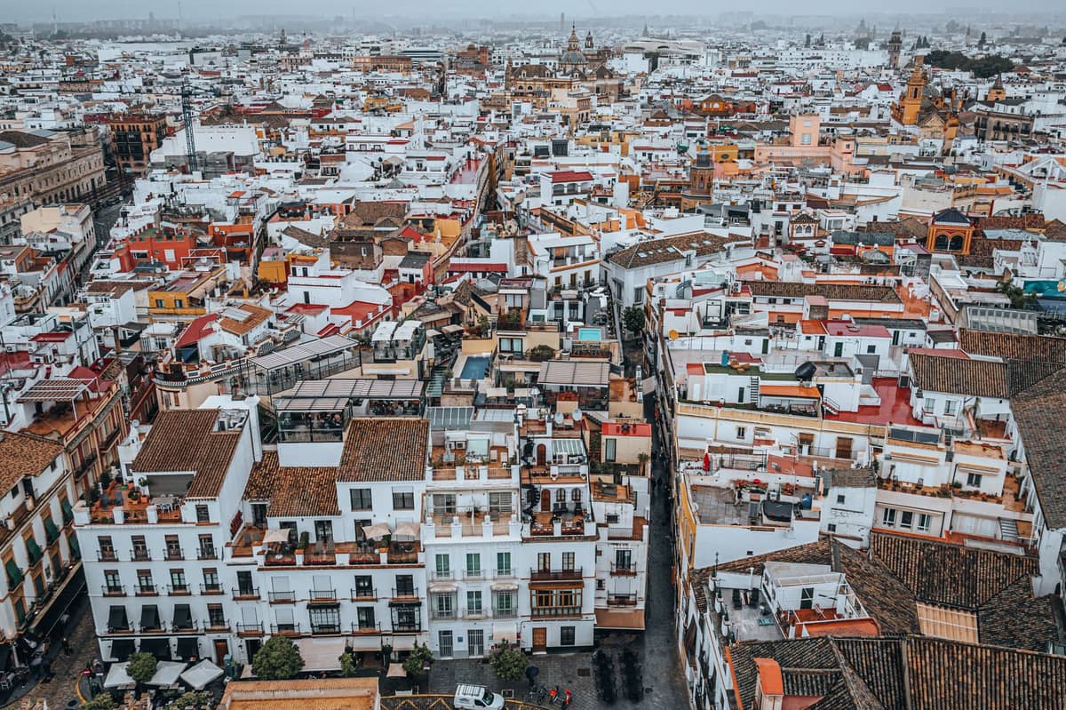 ภาพถ่ายทางอากาศมุมกว้างของใจกลางเมืองเก่าแห่ง Seville ที่มีอาคารทาสีขาวแน่นขนัดภายใต้ท้องฟ้ามีเมฆ