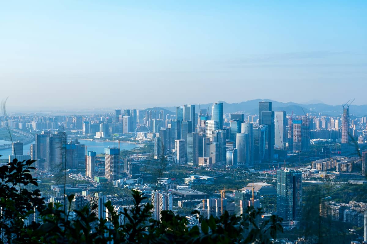 Vista panorâmica diurna sobre o horizonte de Shenzhen com arranha-céus, céu limpo e colinas ao fundo, destacando o clima costeiro subtropical da cidade.