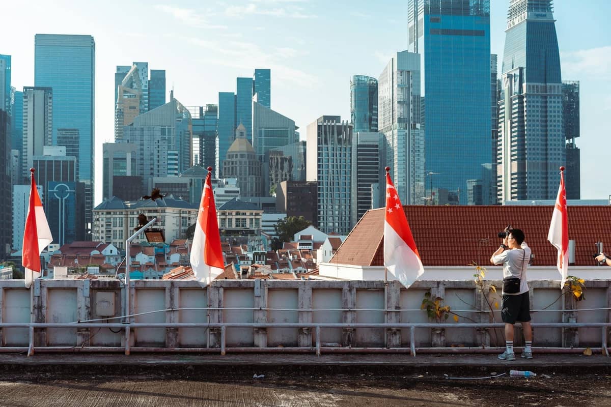 A traveler photographs the Singapore skyline from a rooftop lined with national flags, capturing the city’s diverse architecture.