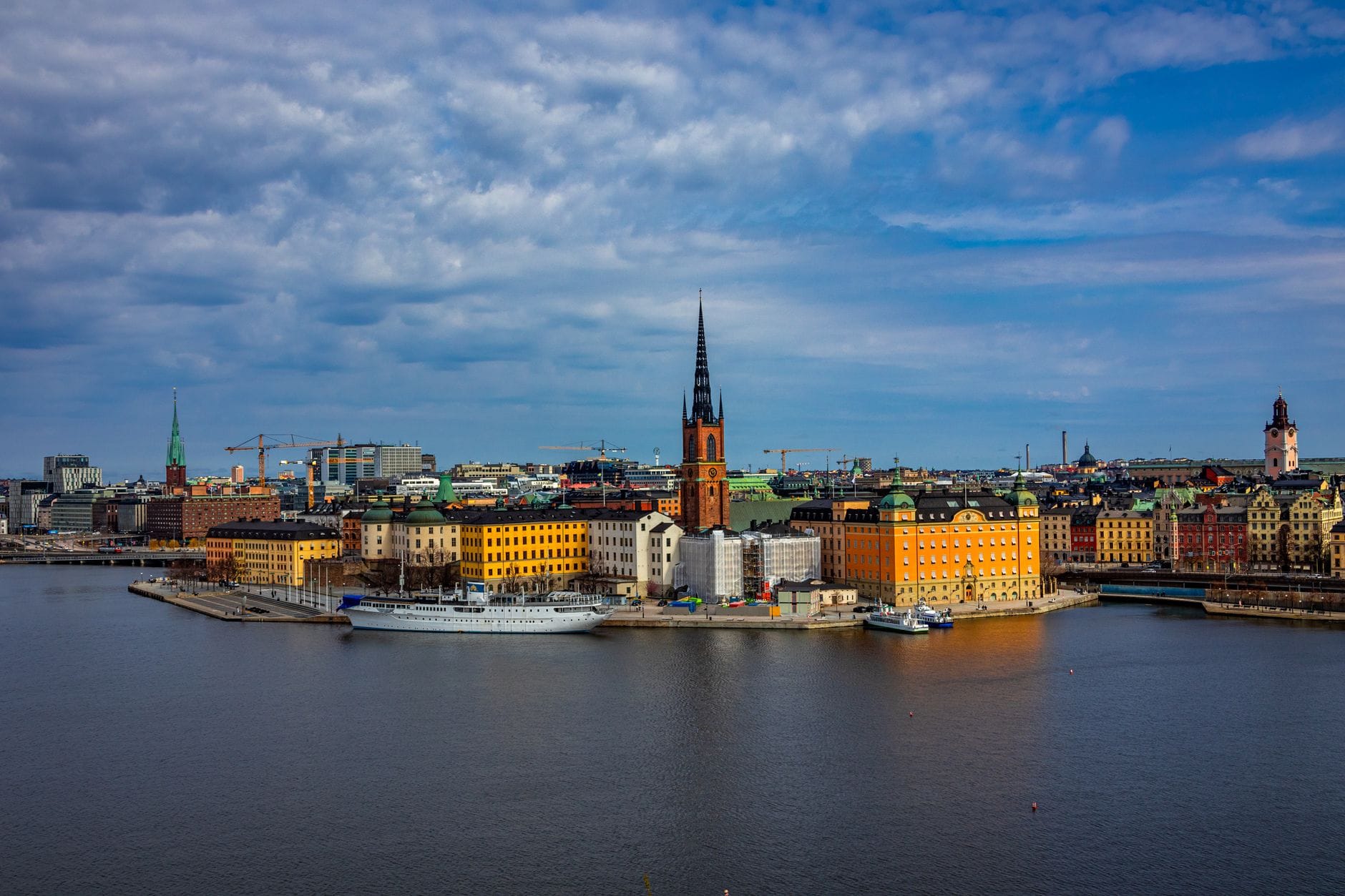 วิวพาโนรามาของริมน้ำเมืองเก่า Stockholm พร้อมอาคารหลากสีสัน ยอดแหลม และท้องฟ้ามีเมฆที่สะท้อนภูมิอากาศของเมือง