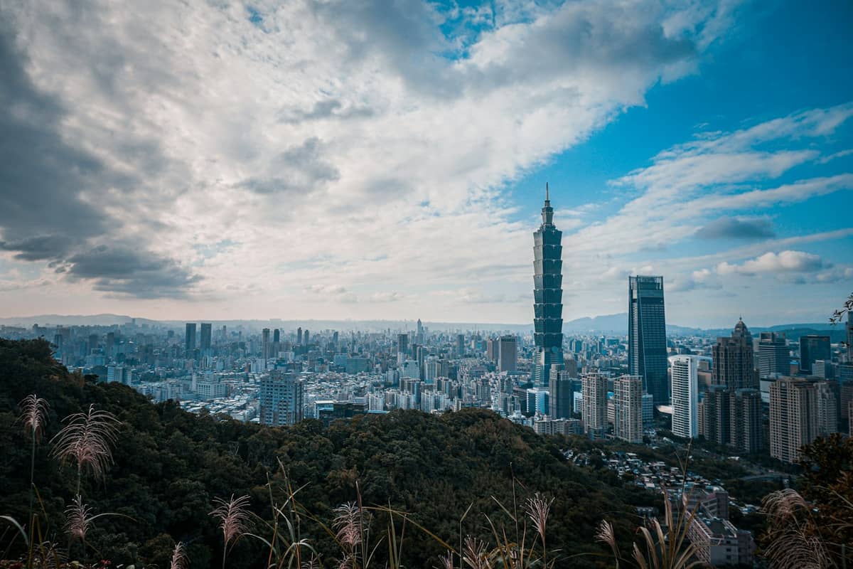 Weitblick auf die Skyline von Taipei mit dem Taipei 101, vielen Stadtgebäuden, bewaldeten Hügeln und dramatischen Wolken am Himmel