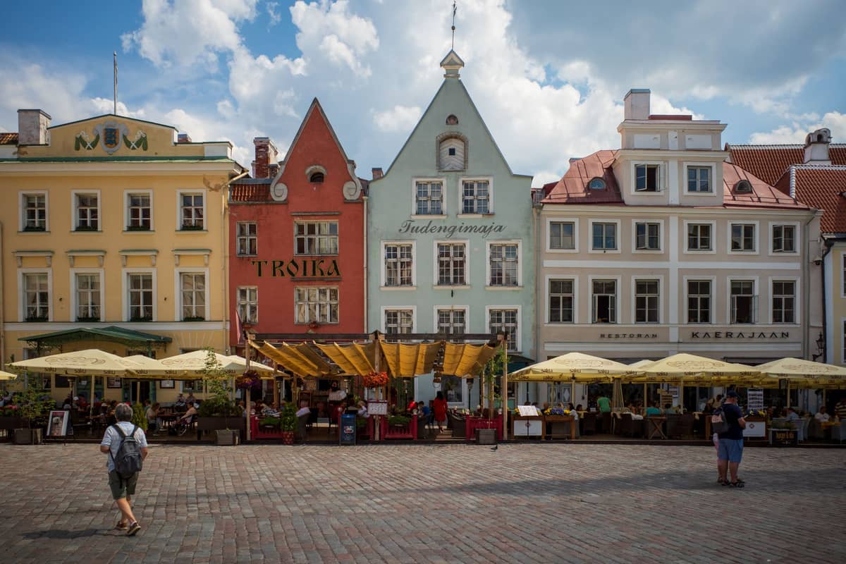 Plaza principal de Tallinn con coloridos edificios medievales y concurridas terrazas al aire libre llenas de gente en un soleado día de verano.